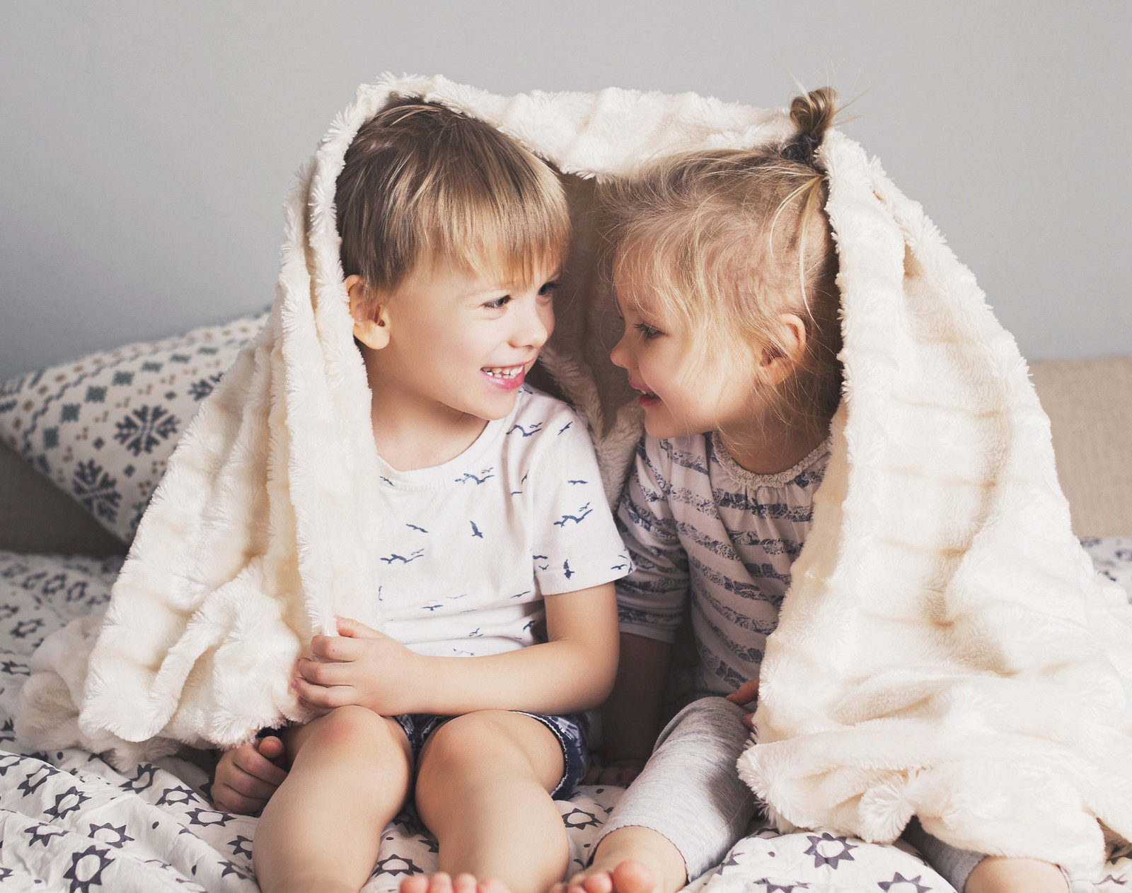 Two siblings laughing together under a cozy blanket
