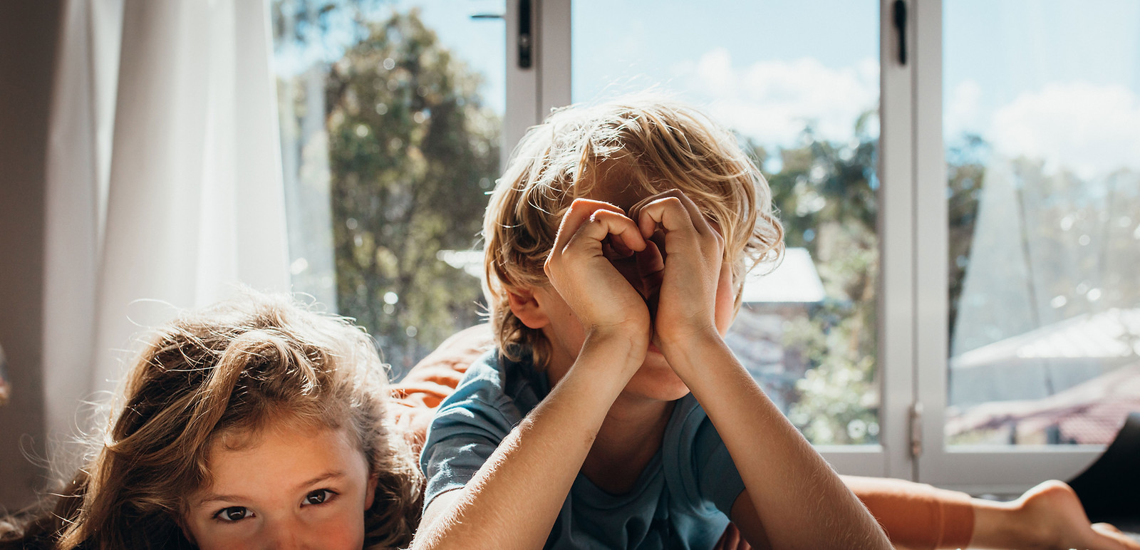 Two young siblings looking forward together, one peering through his hands like a telescope